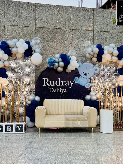 For Baby Rudray's Kuan Poojan ceremony, we designed this chic and modern backdrop. A shimmering silver sequin wall is framed by stylish blue, white, and silver balloon arches, complete with a cozy couch for photos and marquee 'BABY' blocks.