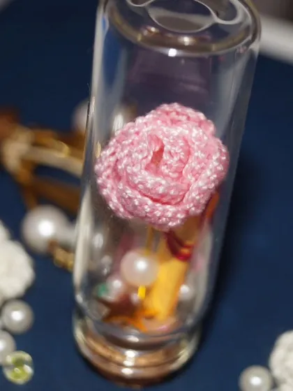A macro shot of a single pink rose inside a glass bottle, showcasing the delicate craftsmanship of this tiny keepsake.