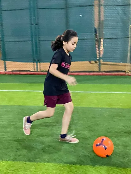 We welcome girls and boys to all our batches. Here, a young female player confidently dribbles the ball, working on her close control and movement during a football drill.