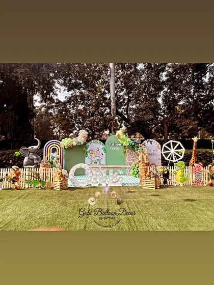 A "Wild One" first birthday stage set up on an artificial lawn, featuring cute animal props and a picket fence.