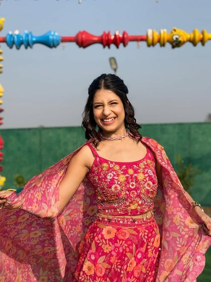 A happy client enjoying the vibrant pink floral cape set. The detailed embroidery on the blouse adds a touch of handcrafted luxury to this playful and festive rental outfit.