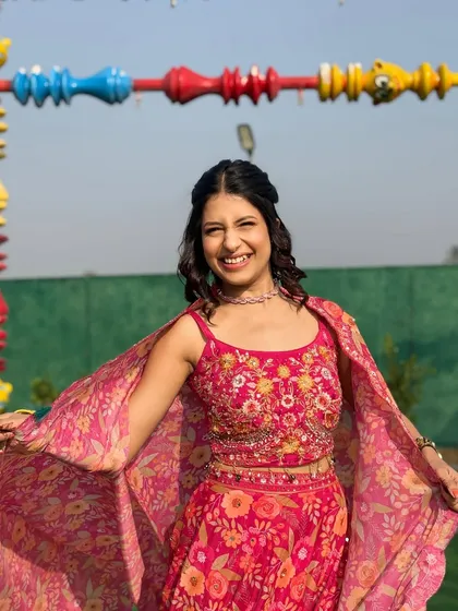 A happy client enjoying the vibrant pink floral cape set. The detailed embroidery on the blouse adds a touch of handcrafted luxury to this playful and festive rental outfit.
