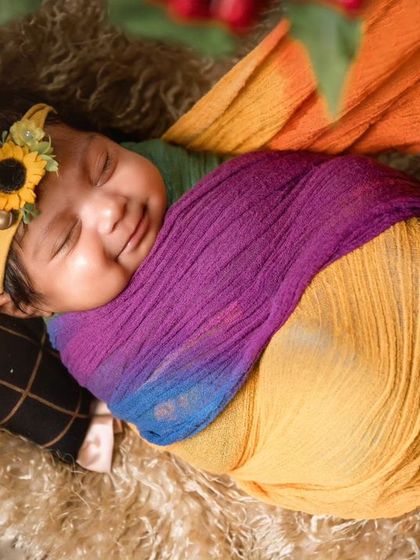 A smiling newborn wrapped in a colorful rainbow swaddle with a sunflower headband, creating a bright and cheerful portrait.