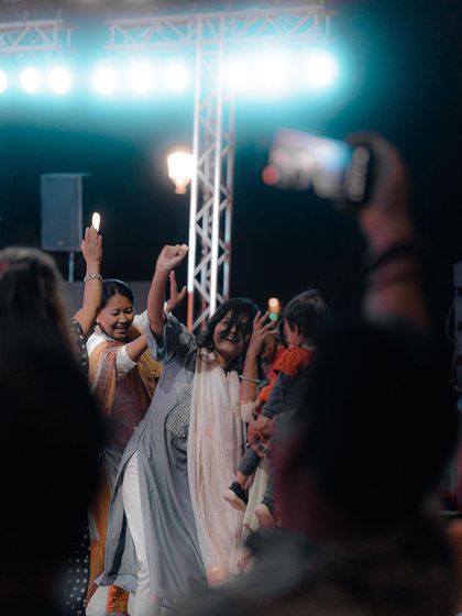 A woman holding a child dances joyfully amidst the crowd at a festival. This heartwarming image captures the family-friendly and inclusive atmosphere of many Delhi events.