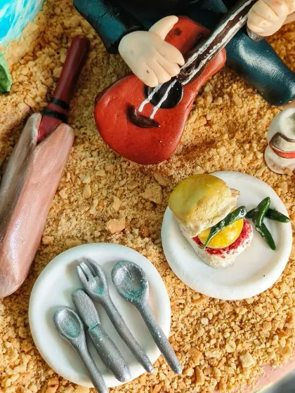 A close-up of the beach scene, showing the tiny vada pav, cricket bat, and cutlery set, all handcrafted from fondant.