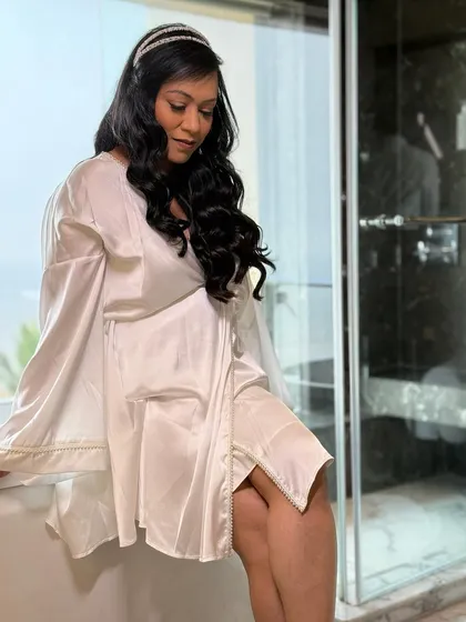 A quiet moment before the ceremony. The bride is relaxed and glowing in her silk robe, her hair styled in soft, romantic waves.