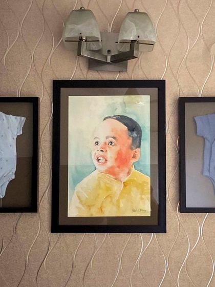 The final display of the child's portrait, beautifully framed between his first onesies. This is a wonderful example of how to turn a commissioned painting into a deeply personal piece of family history.