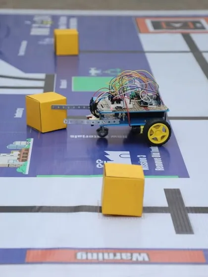 A close-up of a line-follower robot navigating a complex track with yellow blocks as obstacles. Building this robot teaches students about infrared sensors, differential drive, and programming logic.