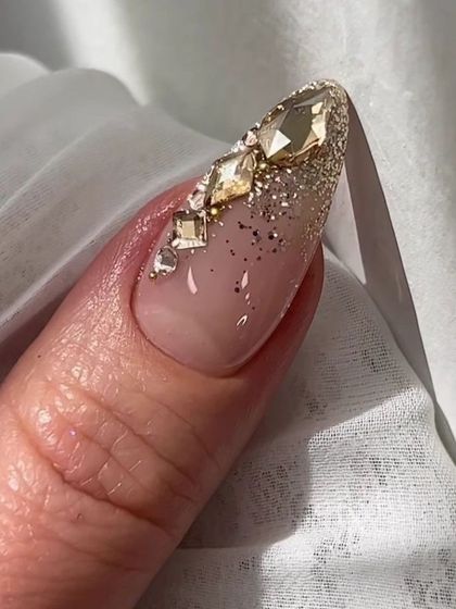 Nail inspiration showing a close-up of a nail heavily embellished with gold glitter and large crystals.