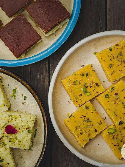 A beautiful flat lay of some of our most popular Diwali sweets. You can see our Kesar Pista Barfi, Chocolate Barfi, and Rose Barfi, all ready to be packed into festive boxes.