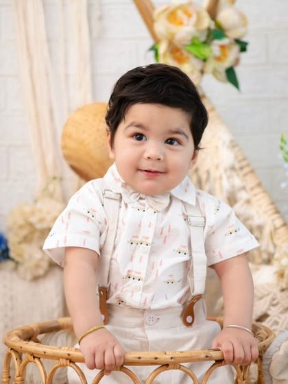 A close-up of a handsome little man in a boho-inspired setting. The soft textures of the wicker basket and surrounding flowers create a gentle and natural portrait.