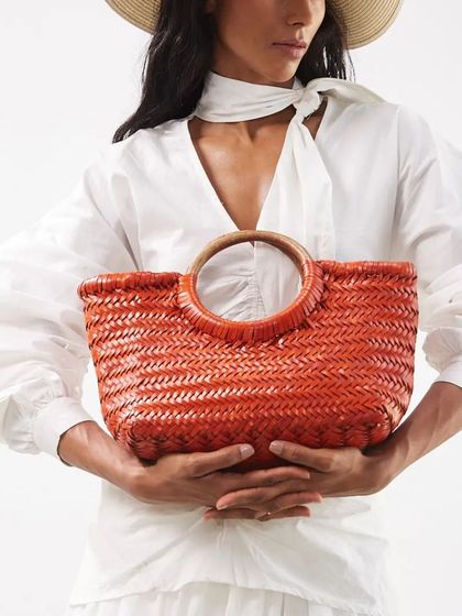 A pop of summer color with our handwoven Gambino Clutch in Mandarin orange. The vibrant hue and wooden handles make it a perfect accessory for a sunny day.