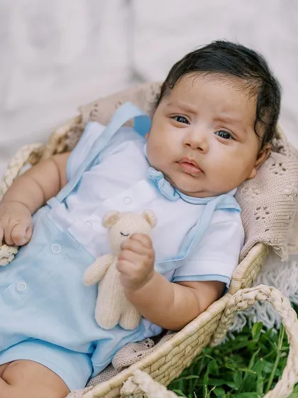 A close-up of the baby in the basket, holding a small teddy bear. Even at a few weeks old, their little personalities start to show.