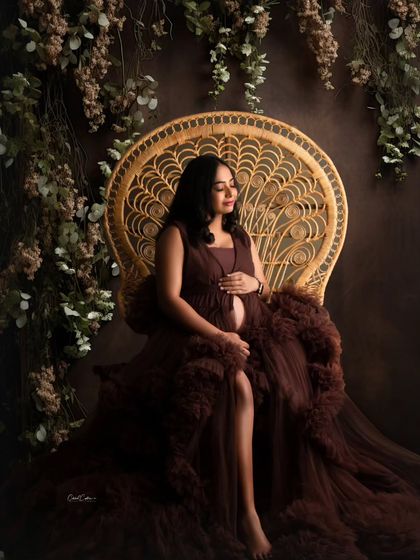 A serene moment on the peacock chair. The mom-to-be is surrounded by lush greenery, wearing a rich brown tulle gown.
