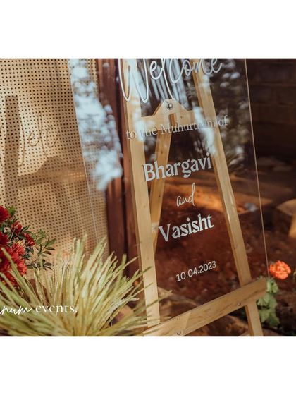 A modern acrylic welcome sign on a wooden easel, contrasting beautifully with the rustic rattan backdrop.