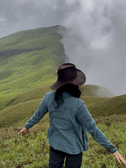 A trekker spreads her arms, embracing the stunning view of the Netravathi ridge line disappearing into the mist.