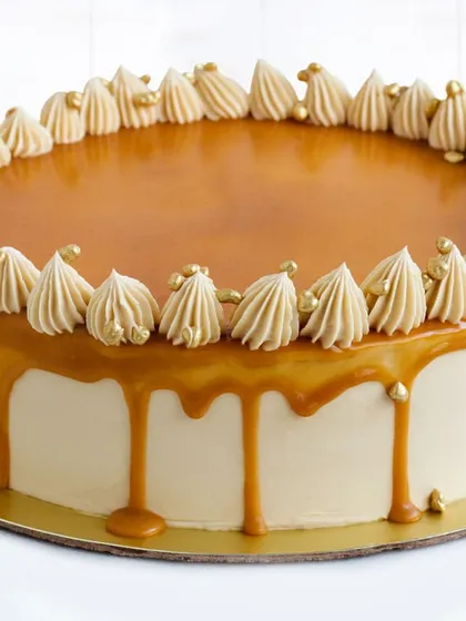 Our elegant Salted Caramel Cake, featuring a smooth buttercream finish, a luscious caramel drip, and a border of perfectly piped rosettes. Each rosette is dotted with a gold sprinkle for a touch of luxury.