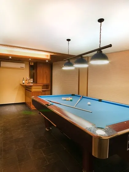 This entertainment room features a classic pool table, a built-in wooden bar, and warm, focused lighting. It's a dedicated space we designed for leisure and socializing with friends and family.