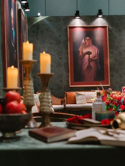 A tablescape detail with candles and fruit, set before a large Raja Ravi Varma painting. The composition of the shot itself mimics the artistic style of the event's inspiration.