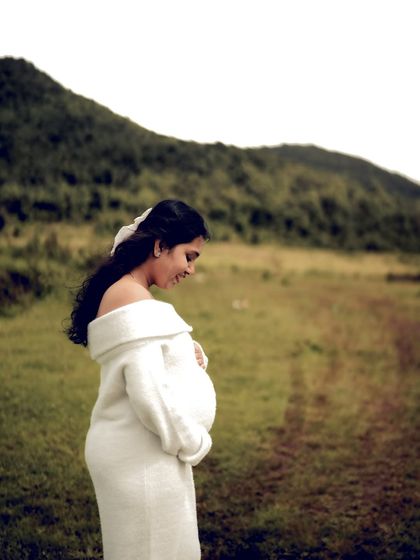 A beautiful solo portrait of the mom-to-be in a white sweater dress, cradling her bump against a backdrop of rolling hills.