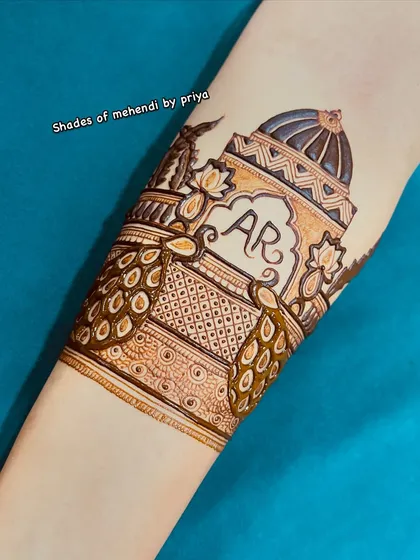 A detailed forearm band featuring peacocks and an architectural dome with the couple's initials 'AR'. This is a great way to personalize a traditional design.
