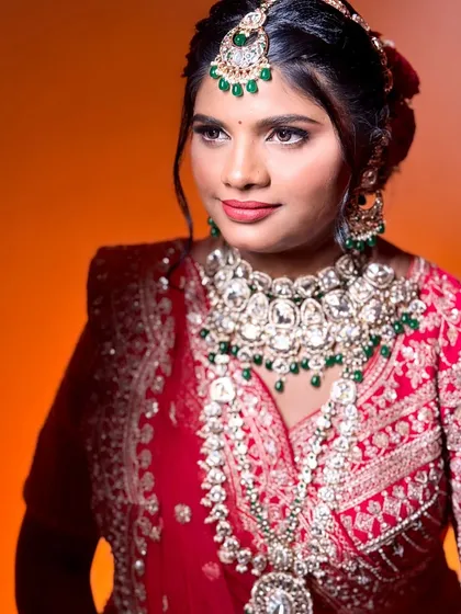 A regal portrait of the bride. The makeup is bold yet elegant, matching the grandeur of her red and green bridal ensemble.