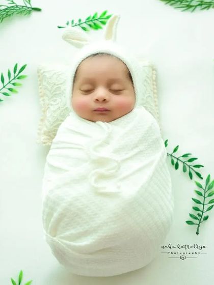 A cute bunny bonnet for this little one, who is swaddled and lying on a tiny pillow, surrounded by scattered leaves for a whimsical touch.
