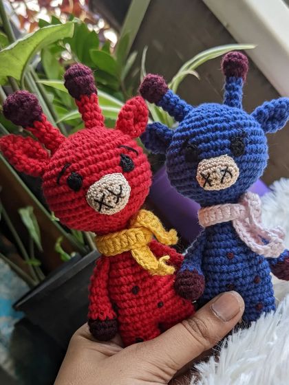 The red and blue giraffes pictured near a window with plants in the background.