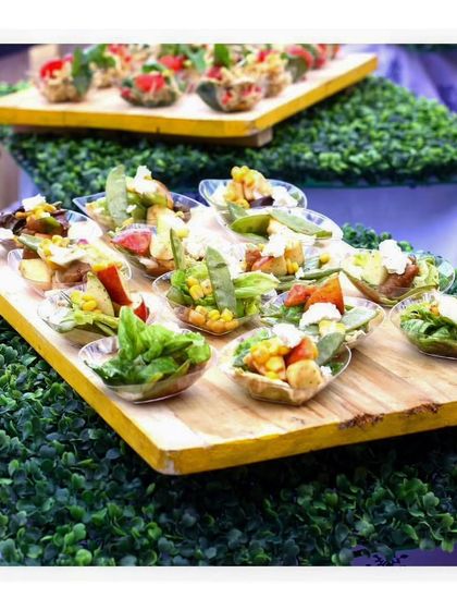A multi tiered display of various salad cups and canapés on a bed of green foliage. This shows how we create appetizer stations that are both abundant and beautifully styled.
