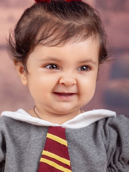 A lovely close-up portrait of a baby girl in her Harry Potter themed outfit, giving a gentle, curious smile.