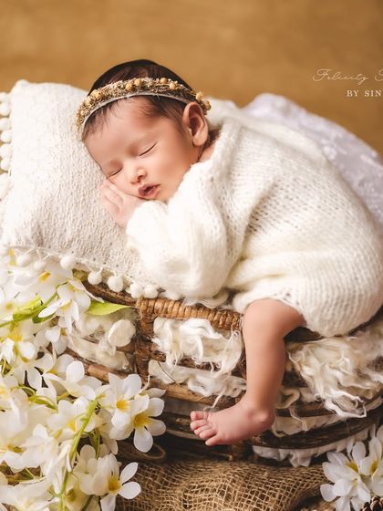 A sleeping angel resting on a stack of rustic baskets, adorned with fresh white flowers. This portrait combines natural textures and soft lighting to create a truly timeless image.