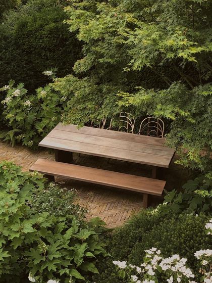 A peaceful dining area tucked away under the canopy of a Japanese maple. The brick patio and simple wooden furniture complement the natural, woodland feel of the garden.