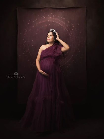 A regal portrait in deep purple. Crowned and poised, this mother-to-be looks out from a celestial backdrop, a true queen in her own right.