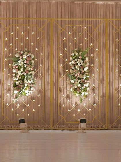 The beauty of minimalistic decor is showcased in this stage design, with simple gold frames, delicate floral bunches, and a backdrop of hanging lights.