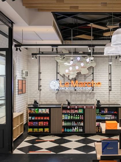 The checkout counter at Le Marche is designed to be a strong brand statement. A map graphic highlights the brand's presence, while the monochrome palette with orange accents reinforces the store's modern and vibrant identity.