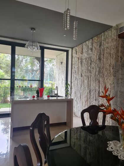 A view from the dining area to the kitchen and garden in our "Mango Tree" house. The design uses a textured stone wall and large glass doors to blend indoor and outdoor living.