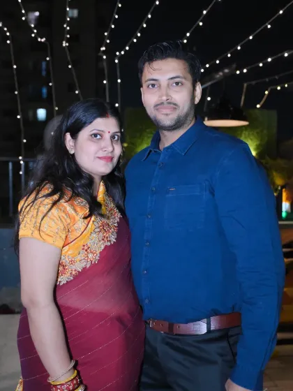 A couple poses for a photo at an evening event with beautiful string lights in the background.