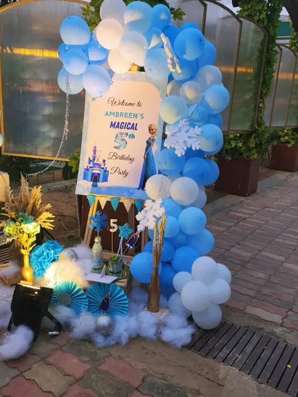The welcome area for the Frozen party. A personalized sign is framed by a blue and white balloon arch, with snowflake details and faux snow on the ground to complete the wintery look.