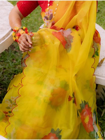 A detail shot of the bride's beautiful yellow floral saree and her henna-adorned hand. A perfect capture of the vibrant colors and details of a Haldi ceremony.