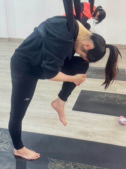 A student uses the hammock for a deep forward fold, stretching the hamstrings and releasing the lower back.