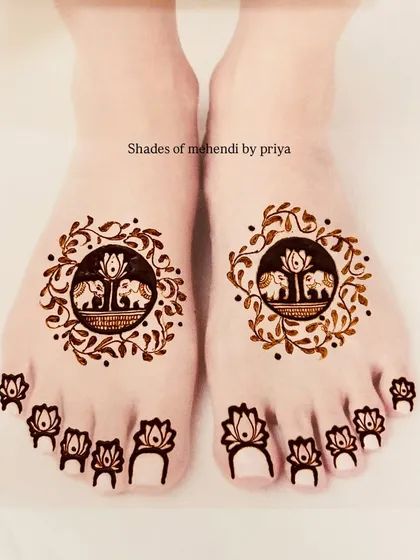 A very cute and minimal foot mehendi design. Each foot has a circular pattern with elephants, framed by leaves, and small lotuses on each toe.
