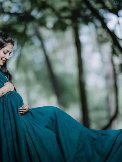 A peaceful solo maternity portrait in the woods. The flowing teal gown pools around the mother-to-be, creating a sense of tranquility and connection with nature.