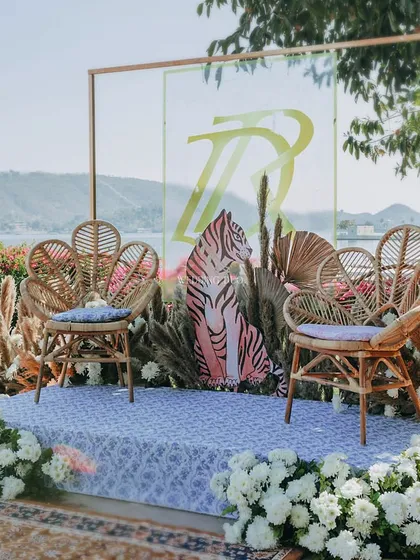 A unique jaimala stage with a wild twist. The couple's seating features peacock-style cane chairs, a custom tiger-print backdrop, and is surrounded by pampas grass and white flowers.