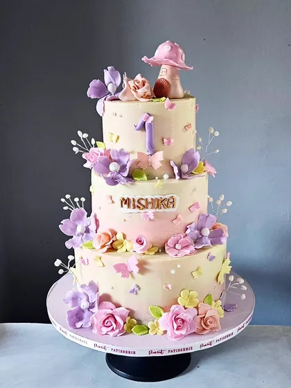 Welcome to an enchanting garden. This three-tier, non-fondant cake was a labor of love, featuring a soft ombré blush, hand-sculpted sugar flowers, delicate butterflies, and a whimsical mushroom topper for a magical first birthday.