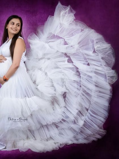 An angel in white. The dramatic, ruffled train of this white gown creates a stunning visual against the rich purple backdrop.