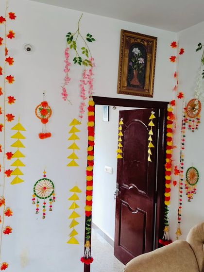 Full view of a living room decorated for a festive Jain occasion. The decor includes door garlands, handmade wall hangings, and paper craft, creating a cohesive and celebratory look.