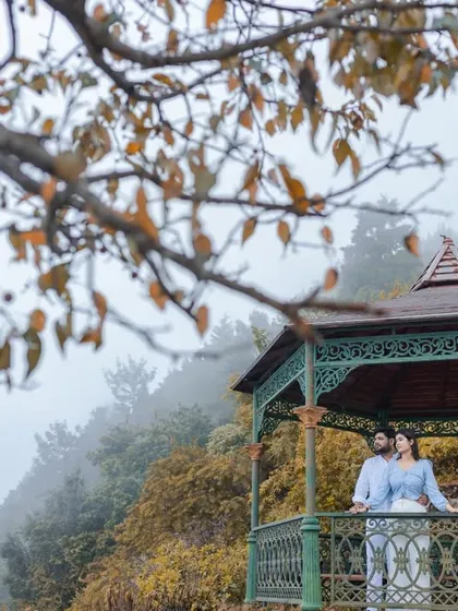 A wide shot showing the couple in the gazebo amidst the misty, atmospheric landscape of Rishikesh. This image captures both the romance of the couple and the beauty of their chosen destination.