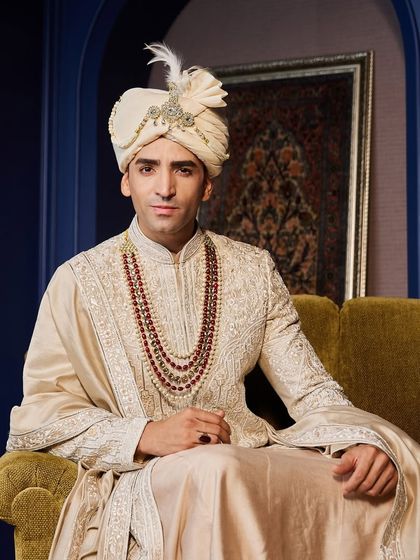 Seated like royalty, this shot captures the grandeur of the sherwani and its accessories. The feathered safa and rich fabrics create an unforgettable image.