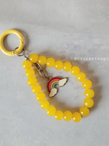 Brighten up your day with this sunny yellow beaded charm. It features a cute rainbow and cloud charm, perfect for adding a cheerful touch to your accessories.