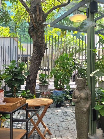 Quiet seating nooks are scattered throughout the garden store. This small corner provides a place to pause, surrounded by lush foliage and curated garden decor, blurring the line between a cafe and a retail space.